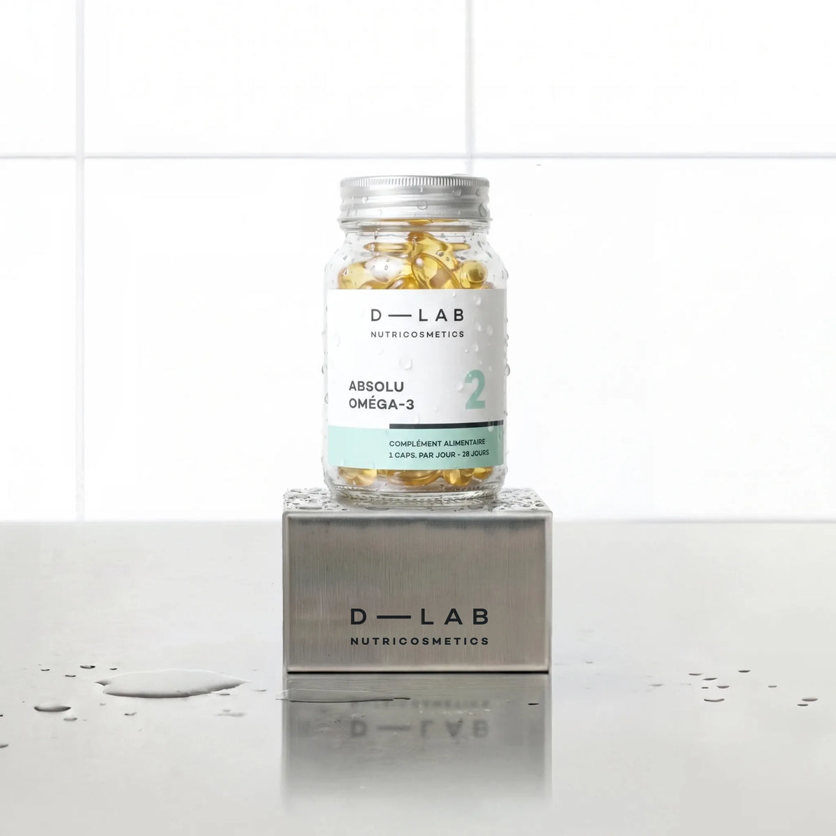 Absolu Oméga-3 D-LAB Nutricosmetics, cure 1 mois : flacon en verre de gélules posé sur un socle inox brossé, fond carrelage blanc