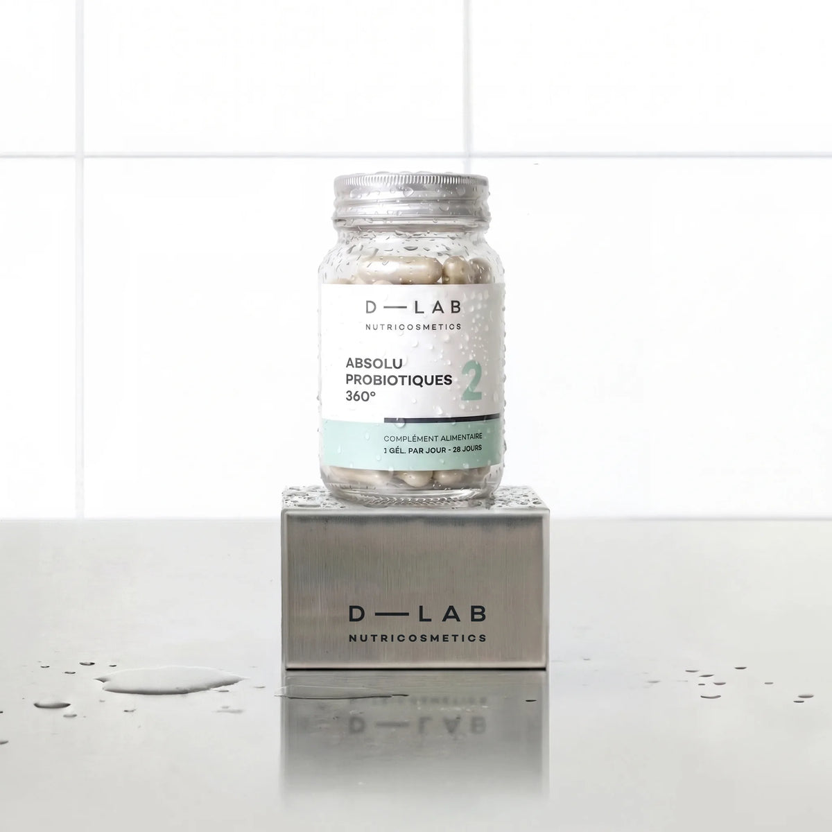 Absolu Probiotiques 360° D-LAB Nutricosmetics, cure 1 mois : flacon de gélules posé sur un socle inox brossé, fond carrelage blanc