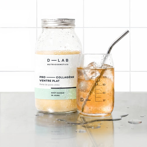 Flacon en verre Pro-Collagène Ventre Plat goût mangue D-LAB et verre glacé de boisson ambrée avec glaçons et paille inox, plan de travail carrelé blanc