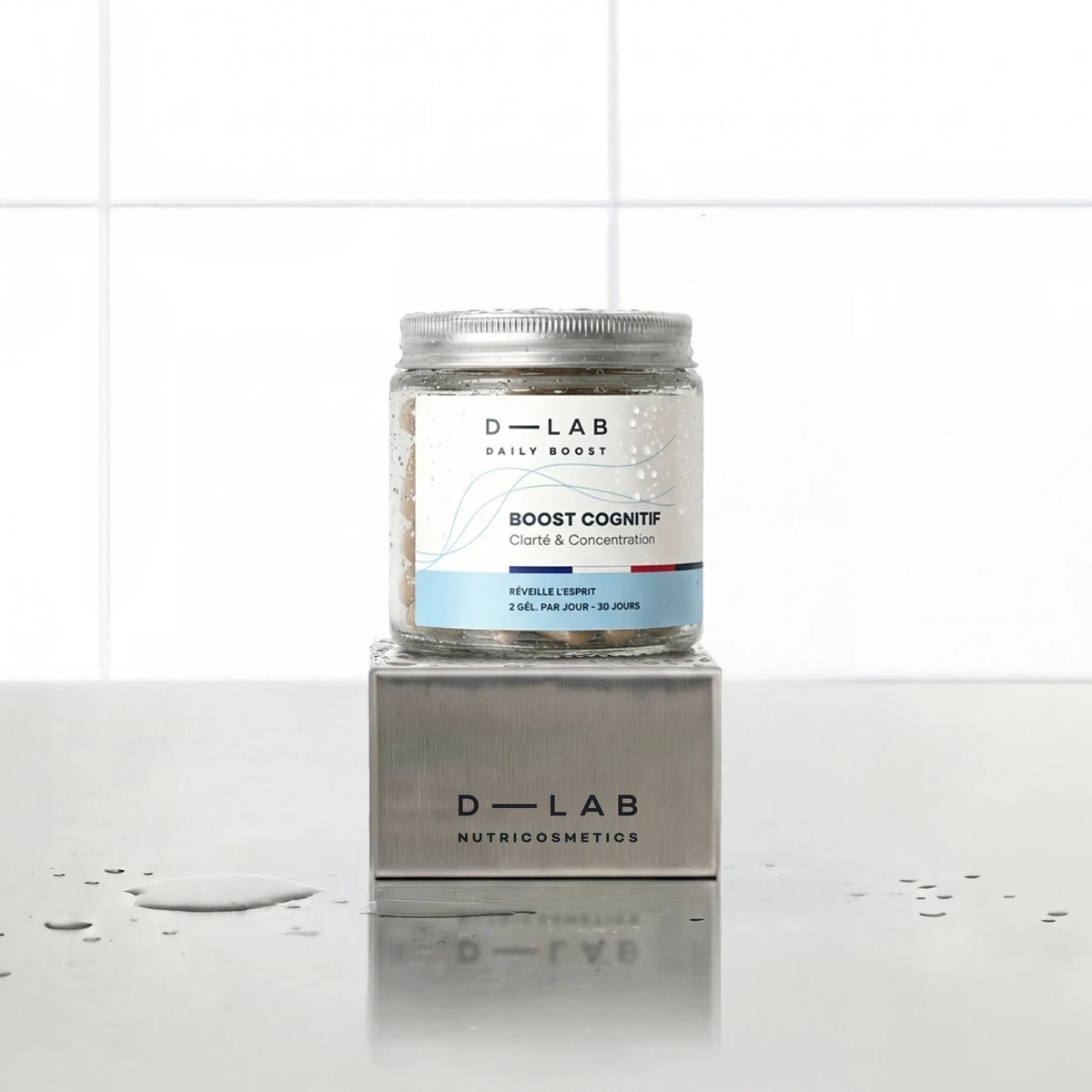 Boost Cognitif Daily Boost D-LAB Nutricosmetics, cure 1 mois : flacon de gélules posé sur un socle inox brossé, fond carrelage blanc
