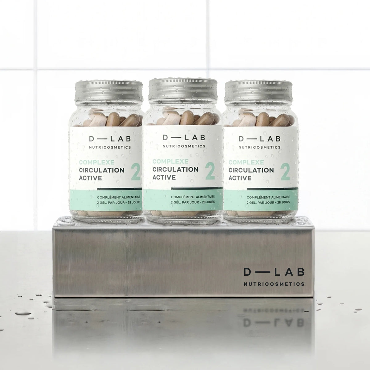 Complexe Circulation Active D-LAB Nutricosmetics, cure 3 mois : 3 flacons de gélules alignés sur un socle inox brossé, fond carrelage blanc