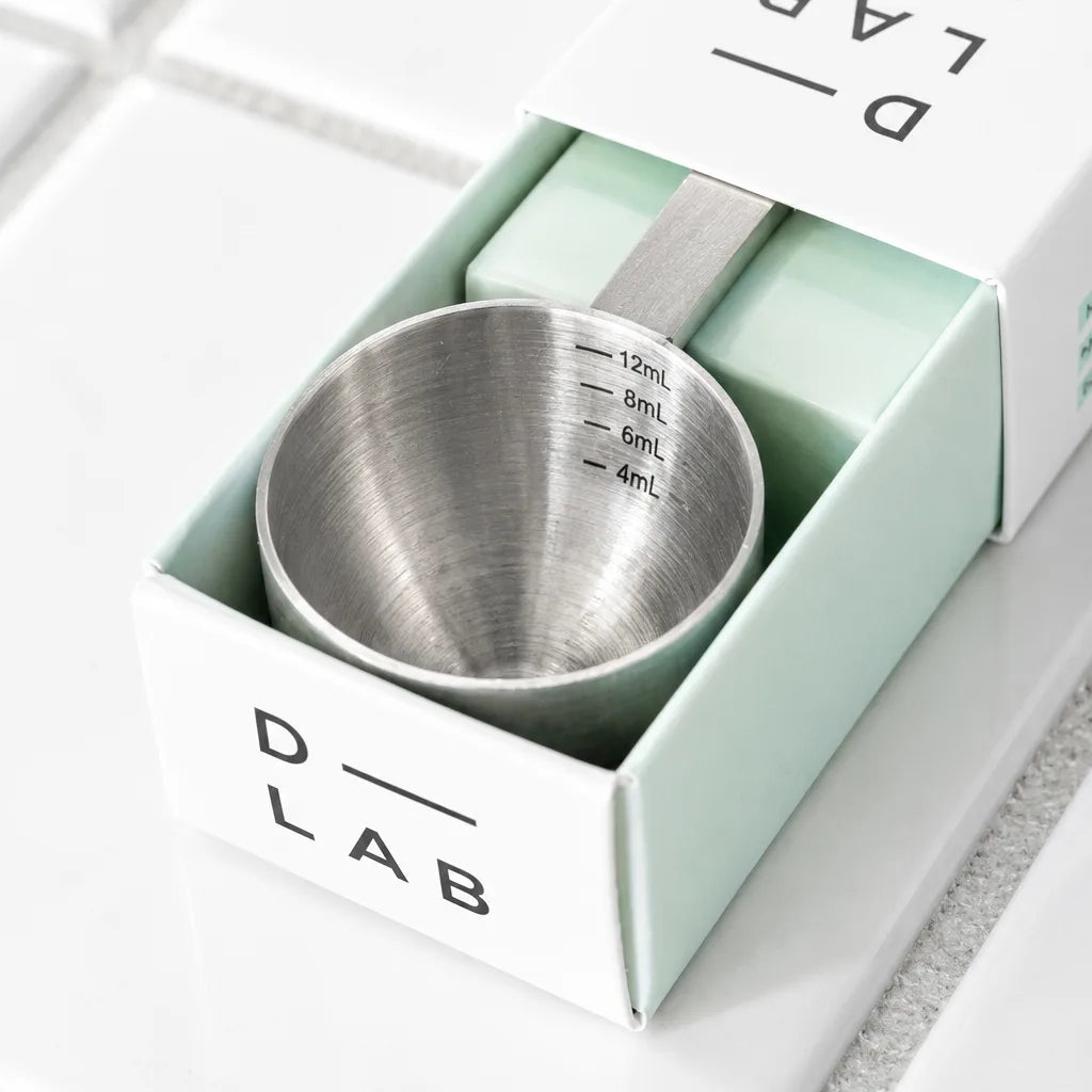 Gros plan sur le godet en inox de la cuillère doseuse D-LAB, graduations 4, 6, 8 et 12 mL, dans son étui vert d'eau