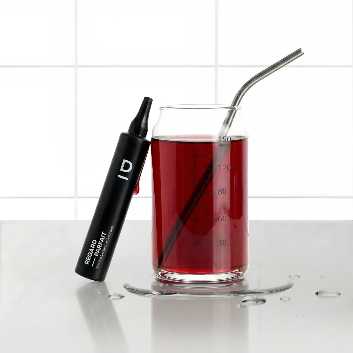 Shots Regard Parfait D-LAB, shot noir posé contre un verre gradué rempli de boisson saveur fruits rouges avec paille inox, fond carrelage blanc
